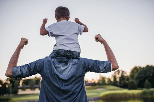 A father carries his young son on his shoulders outdoors at sunset, symbolizing fatherhood, guidance, strength, and the joyful bond between parent and child.