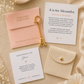 A styled flat-lay of a custom invitation suite from Namestories, featuring a blush pink envelope with gold foil text, a white invitation card with elegant typography, a matching 'Made Especially For' card, and a decorative gold A initial keychain, all arranged on a textured beige fabric background with dried flowers.