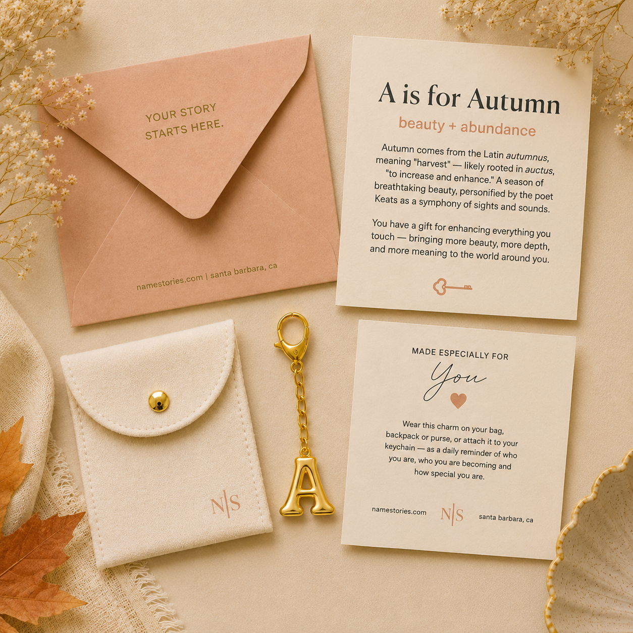 Personalized stationery gift set featuring a peach envelope with gold foil text, a cream fabric pouch with a gold snap, a gold key, and two custom cards on a neutral beige background with autumn-themed props.