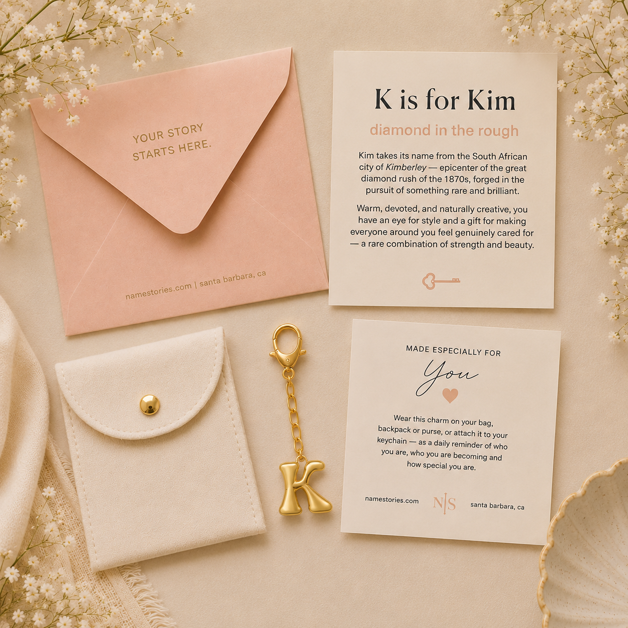 A styled flat-lay of personalized wedding stationery and gift accessories on a textured cream fabric background. The set includes a peach envelope with gold foil text, a cream card reading 'K is for Kim', a cream card with a 'Made especially for You' message, a white leather pouch with a gold snap, and a gold letter K keychain.