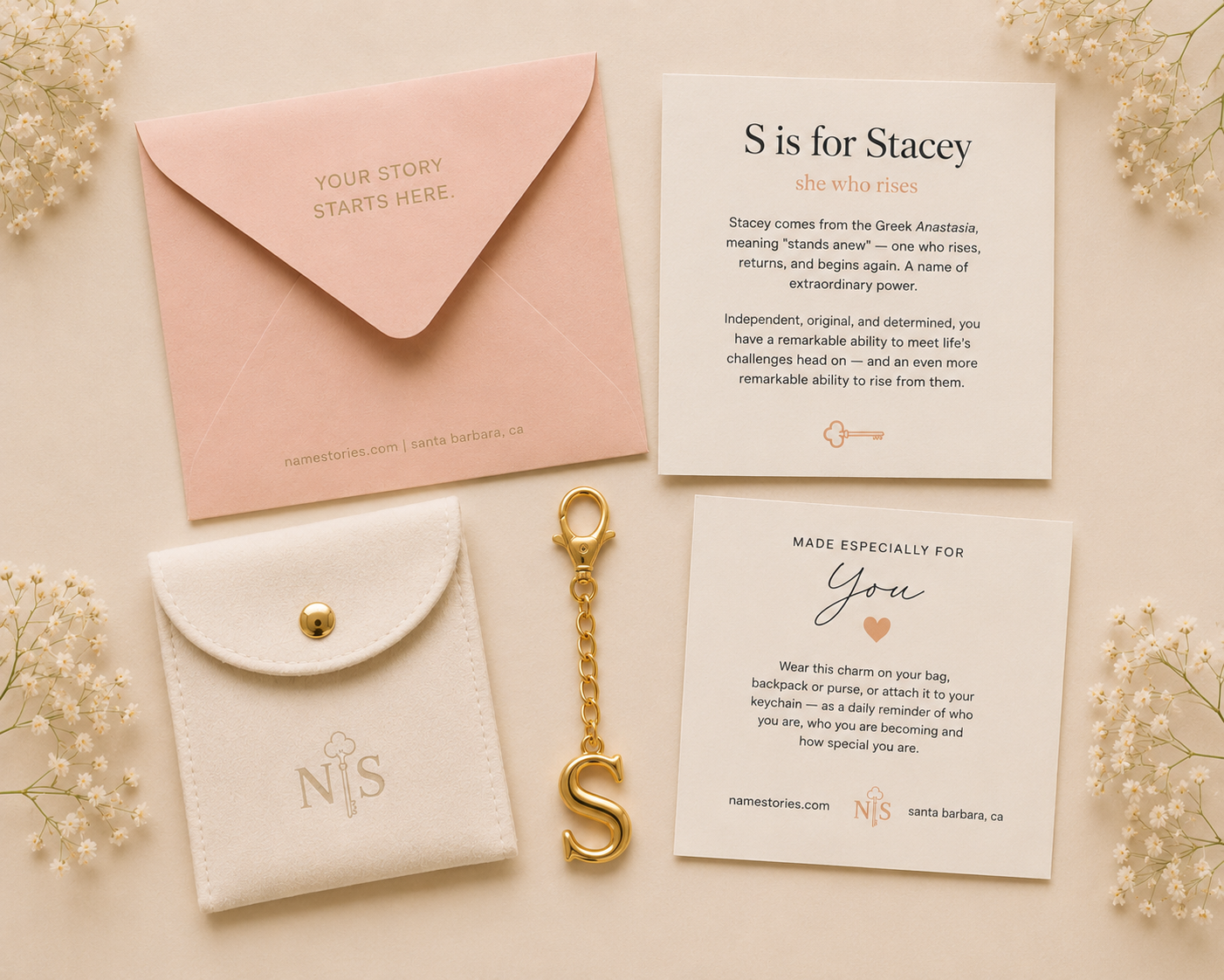 A styled flat-lay of a custom bridal shower gift set on a warm cream background, featuring a pink envelope, a white faux-leather pouch with a gold clasp, a gold keychain with an 'S', and two printed cards.